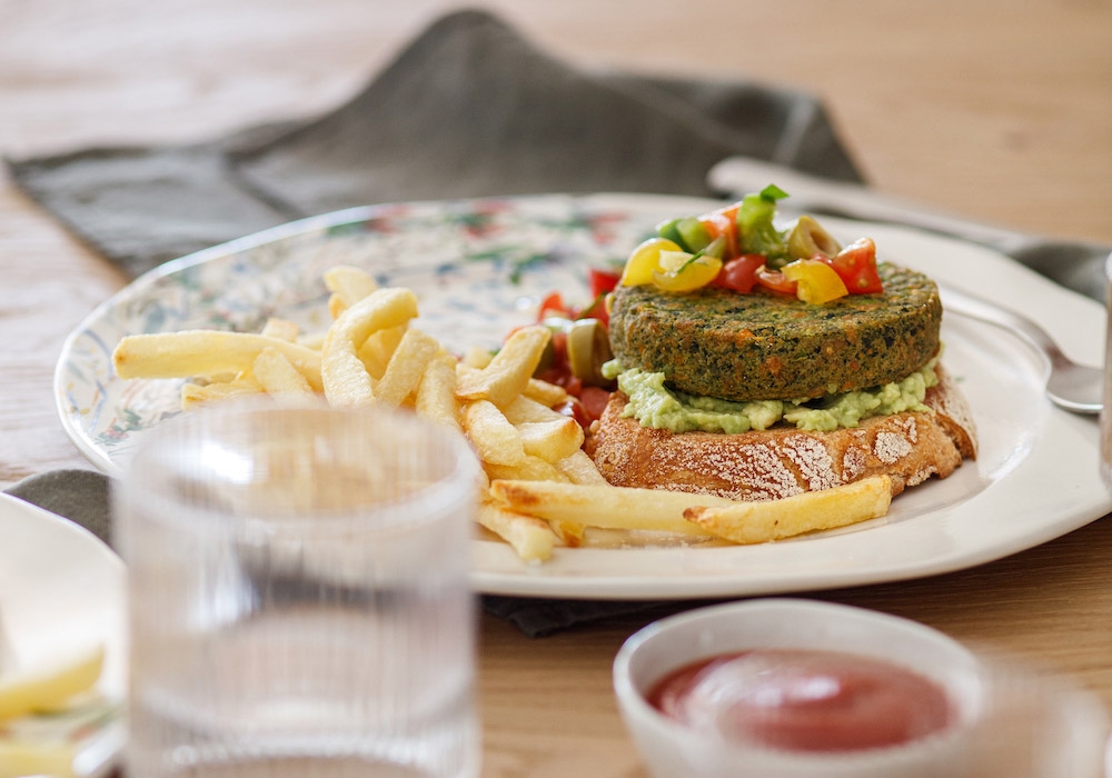 Burger on toasted bread with avocado cream, cherry tomatoes and olives
