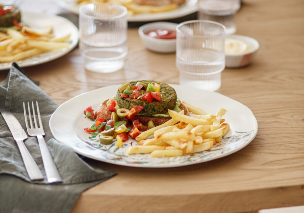 Spinach burger on toasted bread with avocado cream, cherry tomatoes and olives